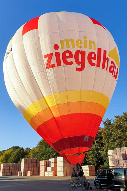 Gäste der 120-Jahr-Feier besteigen den hauseigenen Heißluftballon zu einer Fahrt in abendlicher Lichtstimmung.