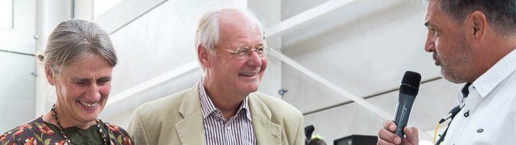 Foto: Angela Thater mit Blumenstrauß, Joachim Thater und der Betriebsratsvorsitzende Ingo Schmidt mit Mikrofon, der dem Ehepaar Thater zur neuen Beton-Fertigteil-Halle gratuliert.